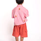 Child wearing a pink shirt and orange shorts on a white background