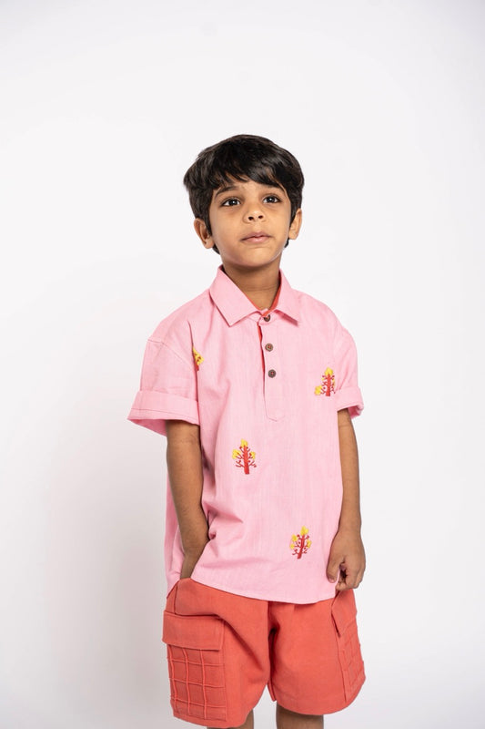 Child wearing a pink polo shirt with floral embroidery and peach shorts on a white background