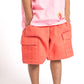 Person wearing a pink shirt with floral designs and coral shorts on a white background