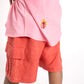 Person wearing a pink sleeveless top with a logo and orange cargo shorts on a white background