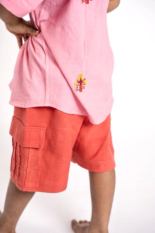 Person wearing a pink sleeveless top with a logo and orange cargo shorts on a white background
