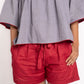 Woman wearing a gray blouse with red trim and red shorts on a white background