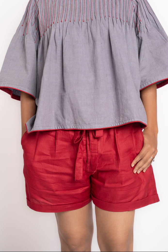 Woman wearing a gray blouse with red trim and red shorts on a white background