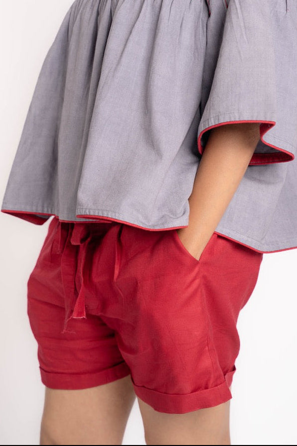 Woman wearing a gray top with red trim and red shorts on a white background