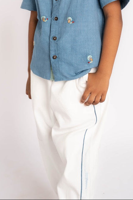 Child wearing a blue shirt with buttons and white pants on a white background