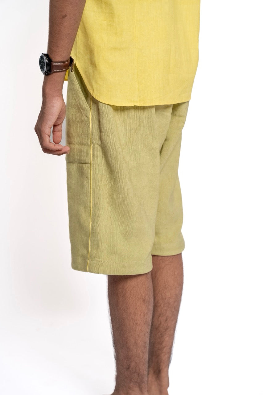 Person wearing light green shorts and a yellow top on a white background